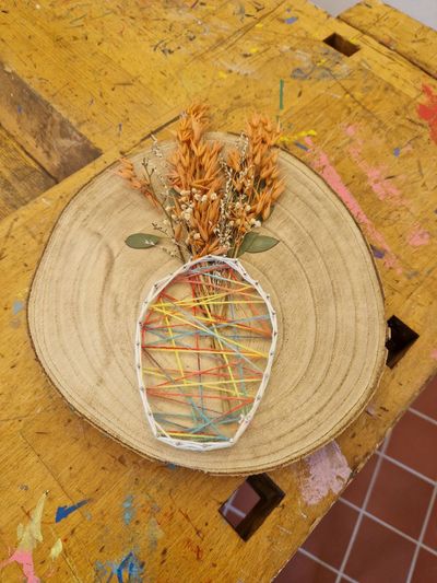 Fadenbild in Vasenform mit Trockenblumen auf einer Holzscheibe